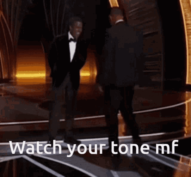 two men standing on a stage with the words watch your tone mf on the bottom