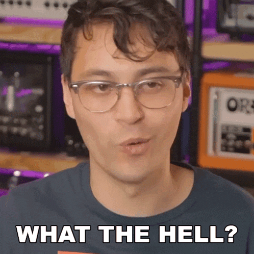 a man wearing glasses and a blue shirt says " what the hell "