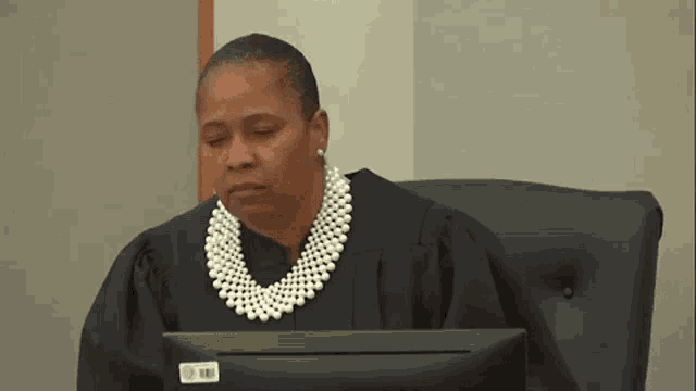 a female judge wearing a pearl necklace and earrings is sitting in front of a computer .