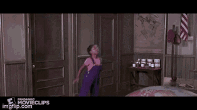 a girl in purple overalls is jumping in the air in a bedroom ..
