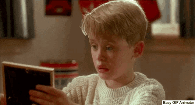 a boy in a white sweater is looking at a picture frame