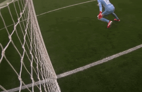 a soccer goalie in a blue uniform is diving to catch the ball
