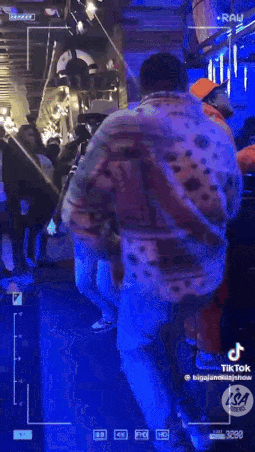 a man in a polka dot jacket is walking in a dark room with a blue light behind him .