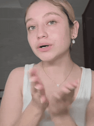 a woman wearing a white tank top and a necklace is clapping her hands