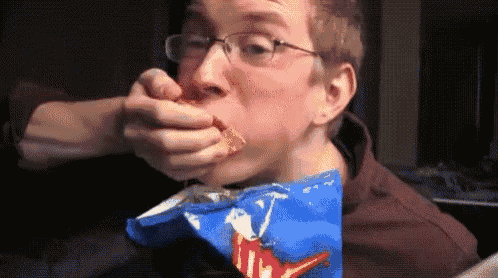 a man wearing glasses is eating a bag of tortilla chips .