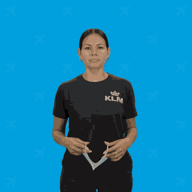 a woman wearing a black klm shirt adjusts her face mask
