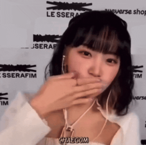 a woman covering her mouth with her hand while wearing headphones and a white shirt with the word chaecom on it
