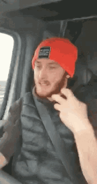 a man wearing a red beanie and a black vest is sitting in the driver 's seat of a car .