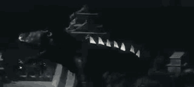 a black and white photo of a dinosaur with sharp teeth in the dark .