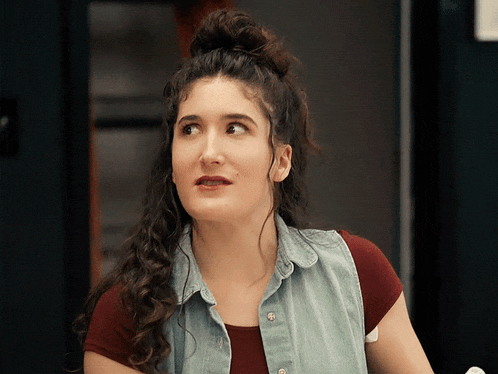 a woman wearing a denim vest and a red shirt is looking up