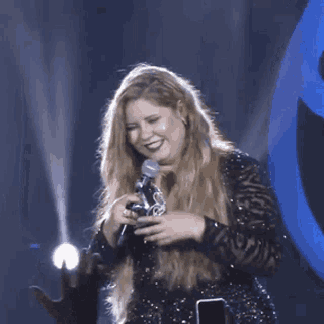 a woman in a black dress is holding a microphone and a trophy