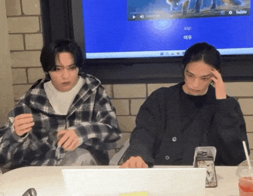 two men are sitting at a table with a laptop and a screen that says youtube on it