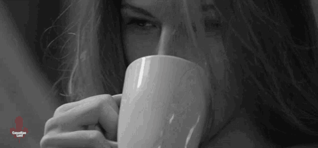a woman is drinking a cup of coffee from a white mug .