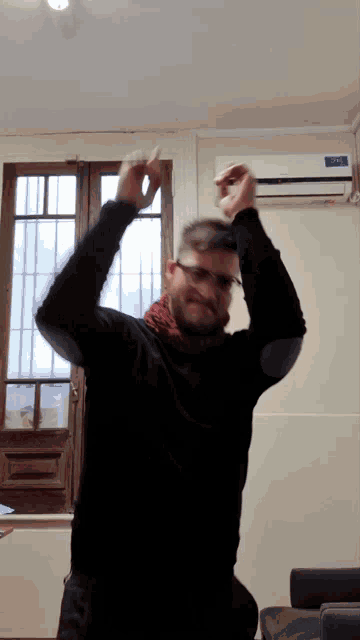 a man wearing glasses and a black sweater is dancing in front of a window