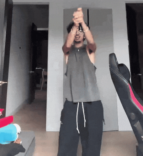 a man in a grey tank top and black pants is standing in a living room holding a remote control