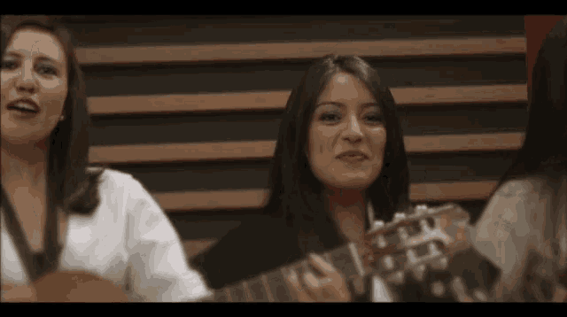 a woman is playing a guitar while another woman sings