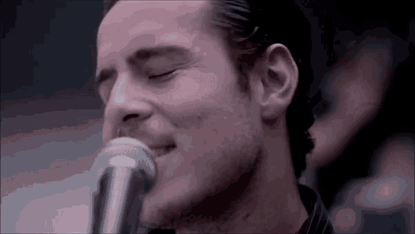 a man is singing into a microphone with his eyes closed and his mouth open .