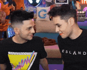 two men are standing next to each other and one of them is wearing a black shirt that says esland .