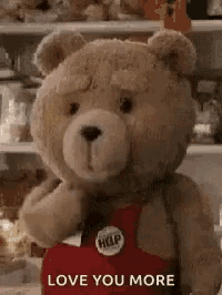 a teddy bear with a help button on his chest is standing in front of a shelf and says `` love you more '' .