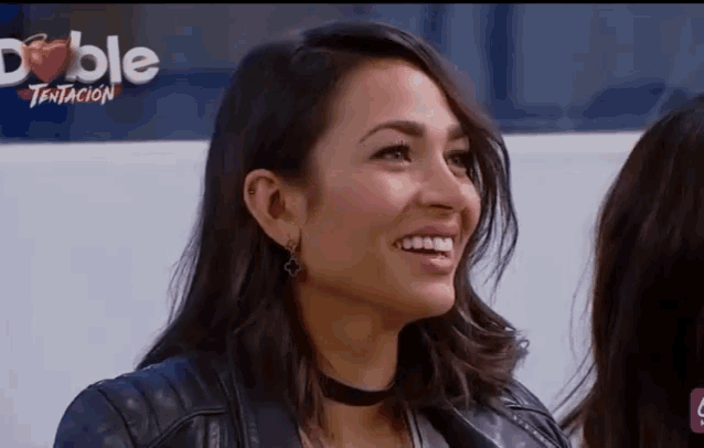 a woman in a black leather jacket is smiling in front of a sign that says doble tentacion