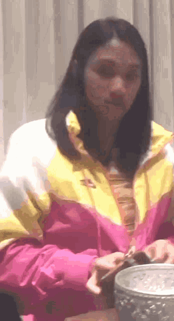 a woman wearing a pink and yellow nike jacket is sitting at a table