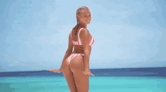 a woman in a pink and white bikini is standing on the beach