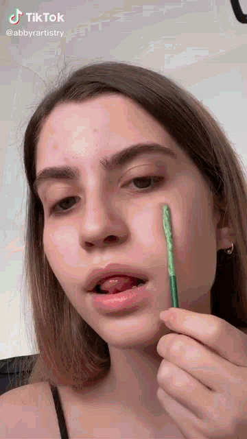 a woman is holding a green stick in front of her face and says tiktok