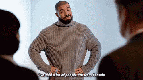 a man in a sweater is standing in front of a group of people and talking .