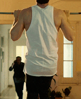 a man wearing a white tank top is doing a pull up