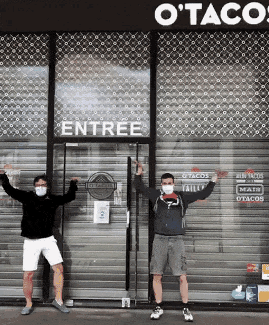 two men wearing face masks stand in front of a store that says o tacos