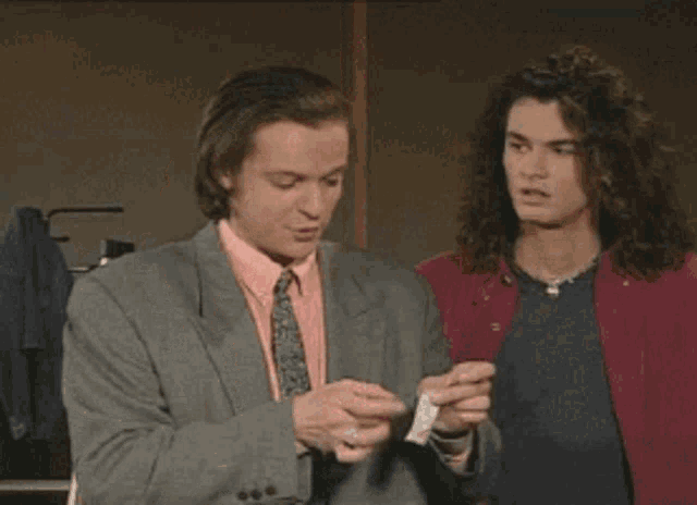 two men are standing next to each other one is wearing a red shirt and the other is wearing a suit