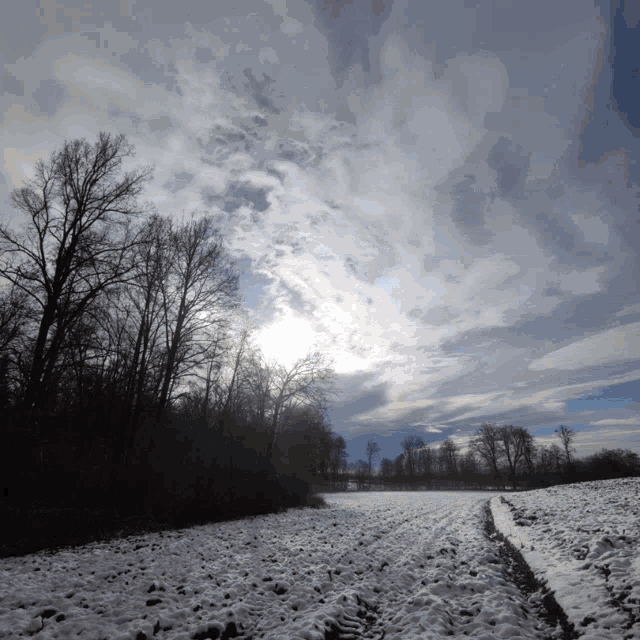 the sun is shining through the clouds above a snowy field