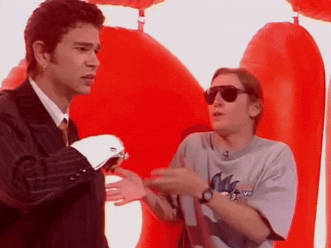 a man in a suit and tie is talking to another man wearing sunglasses in front of a red balloon .