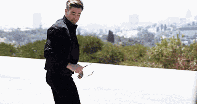 a man in a black jacket and black pants is standing on the side of a road