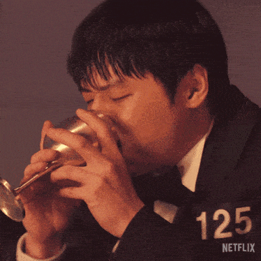 a man is drinking from a glass with the number 125 on his shirt