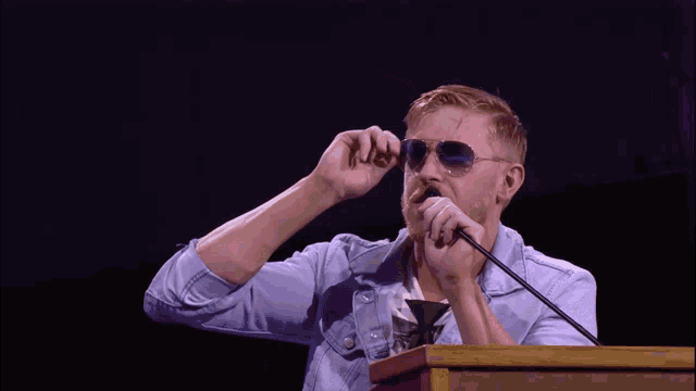 a man wearing sunglasses holds a microphone in his mouth