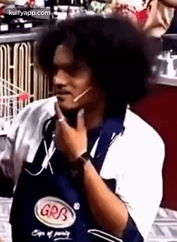 a man with curly hair is wearing a blue apron and a microphone on his head .