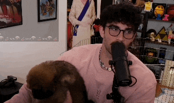 a man wearing glasses and a pink shirt is holding a small brown animal in front of a shure microphone