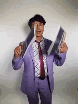 a man in a purple suit and tie is holding a magazine in his hand .