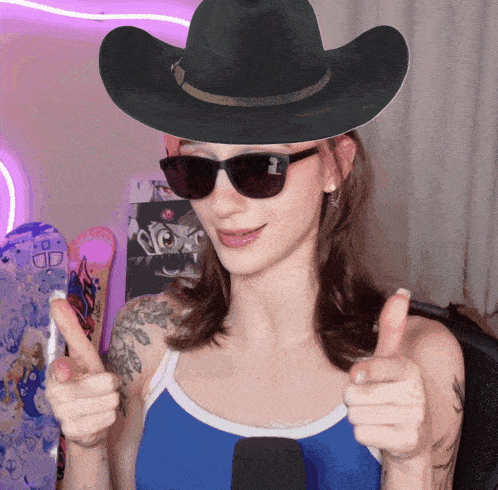 a woman wearing a cowboy hat and sunglasses giving two thumbs up