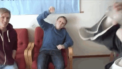 a man in a blue sweater is sitting in a chair with his arms in the air