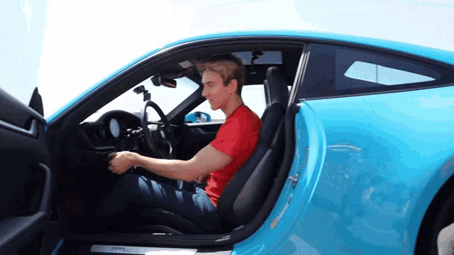 a man in a red shirt is driving a blue car