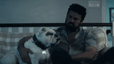 a man with a beard is sitting on a couch with a white dog