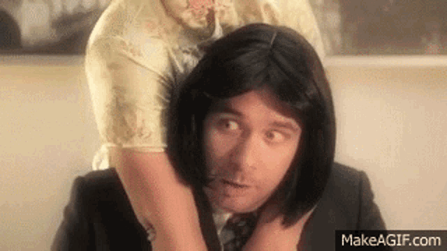 a woman in a wig is holding a man 's neck .