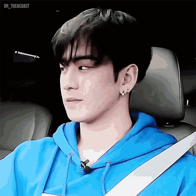 a young man in a blue hoodie is sitting in a car with a seat belt on .