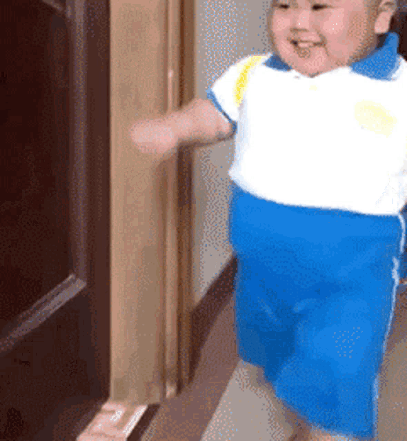 a little boy in a white shirt and blue shorts is walking down a hallway .