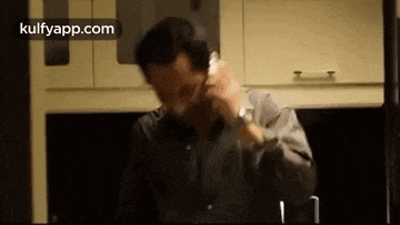 a man is talking on a cell phone in a kitchen while wearing a watch .