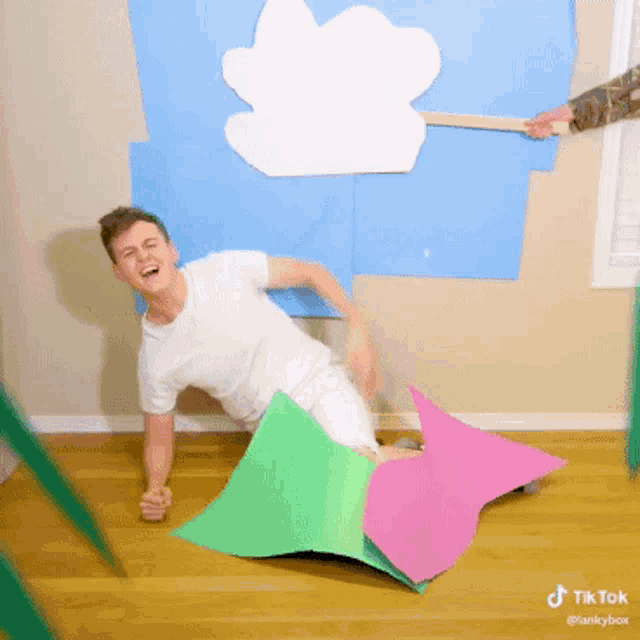 a man is laying on the floor with a pink and green umbrella in front of a blue wall that says tiktok @tankybox