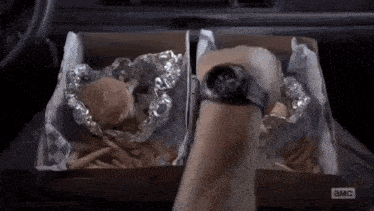 a person is taking a box of hamburgers and french fries out of a car .