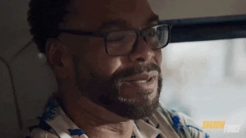 a man with glasses and a beard is sitting in a car and smiling .